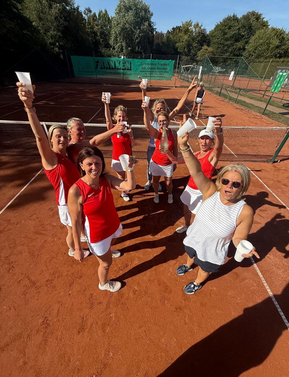 acht Frauen eiern mit Bechern auf einem Tennisplatz