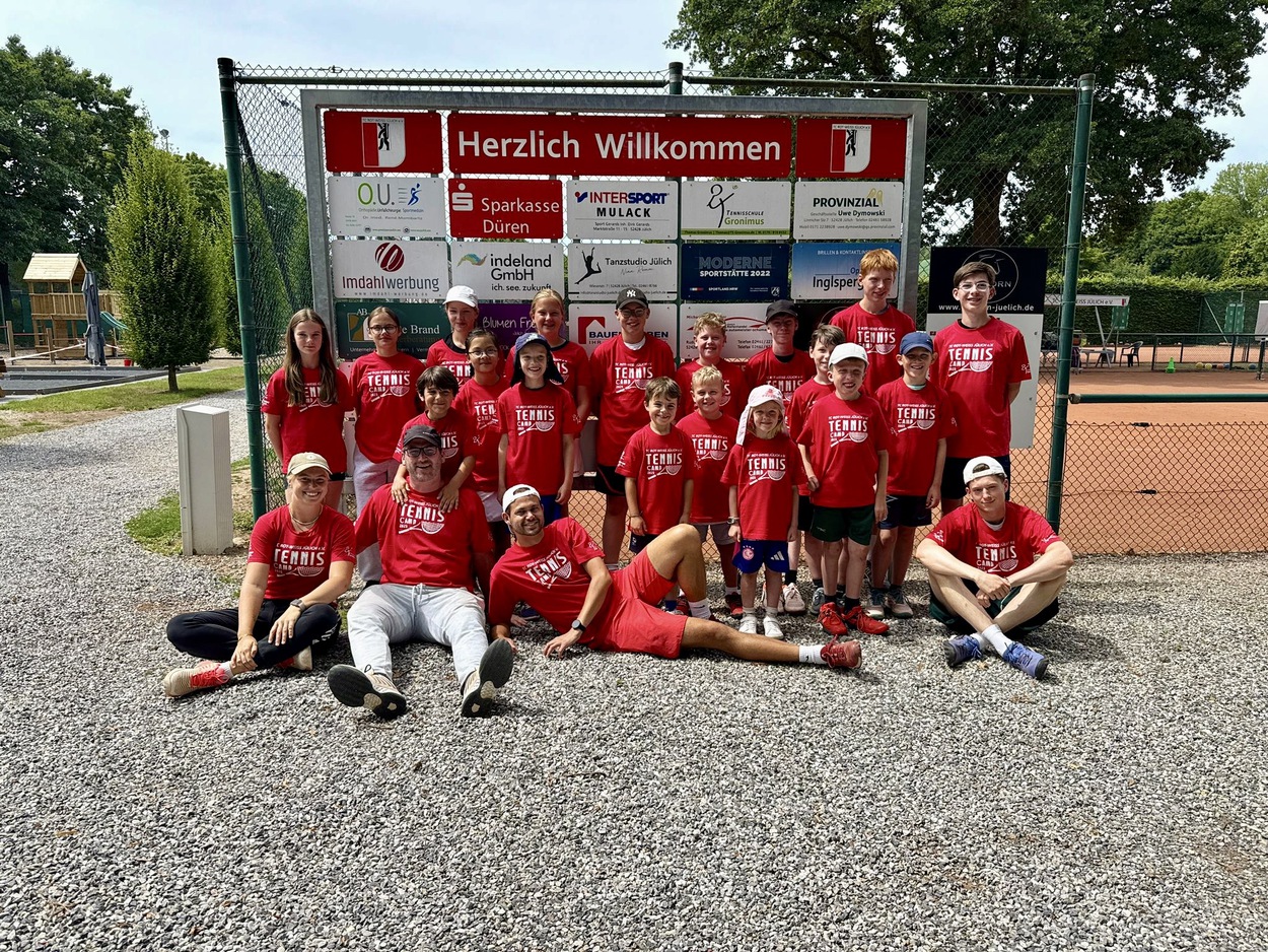 Gruppenfoto von Jugendlichen und deren Betreuern vor einem Tennisplatz, alle mit dem gleichen roten Tshirt
