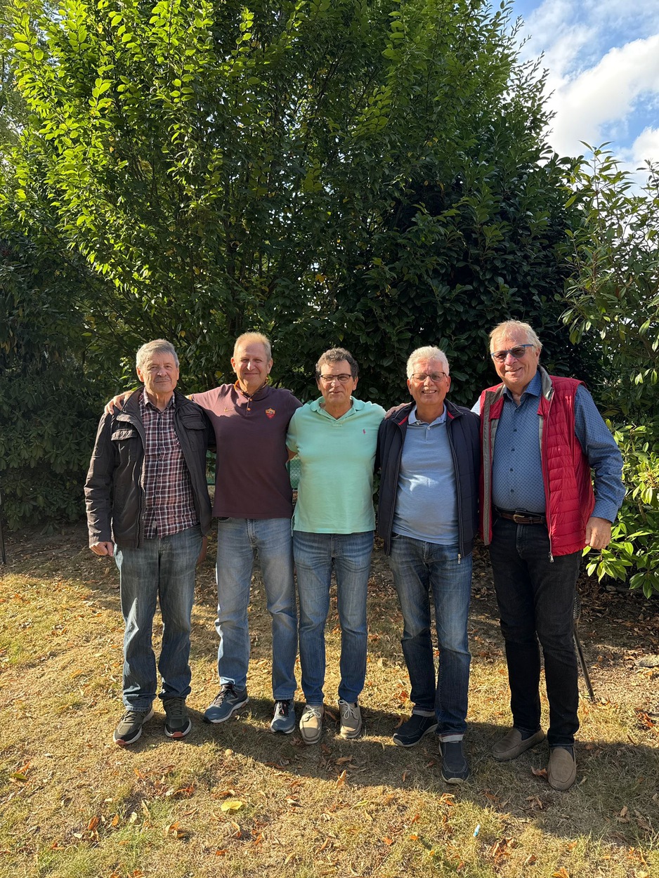 fünf Männer nebeneinander vor einem Busch