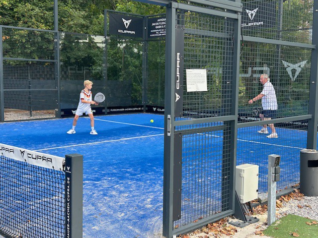 Ein Teenager und ein älterer Mann spielen zusammen als Doppel auf einem Padelplatz